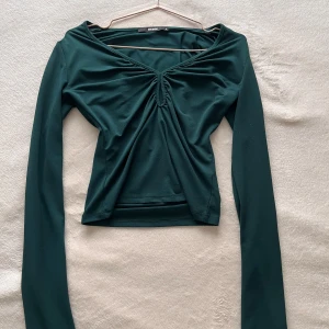 Mörkgrön långärmad topp från Bikbok  - Snygg mörkgrön topp från Bikbok med långa ärmar. Toppen har en v-ringad design och är tillverkad i ett mjukt och stretchigt material som ger en bekväm passform ✨