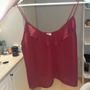 Röd linnetopp från Gina Tricot - Snygg röd linnetopp från Gina Tricot med smala axelband och volangdetalj vid halsringningen. Perfekt för varma dagar eller som ett lager under en kavaj. Enkel och stilren design som passar till mycket.