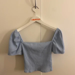 Ljusblå ribbad topp - Säljer en söt ljusblå ribbad topp med puffiga kortärmar. Toppen är croppad och har en fyrkantig halsringning som ger en trendig look. Perfekt för varma dagar!