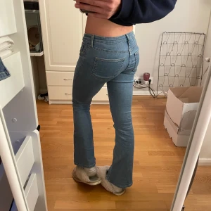 Blå bootcut jeans - Snygga blå bootcut jeans med låg midja. Perfekta för en avslappnad stil. De har en klassisk femficksdesign och en knappgylf. Passar bra till både sneakers och klackar.