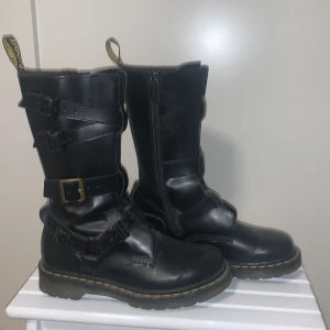 Svarta boots från Dr. Martens - Säljer ett par svarta Dr. Martens boots i skinn med spännen och dragkedja. De har den klassiska gula sömmen. Orginalpris runt 1200kr men har bara använt ett fåtal gånger och vill bara bli av med, storlek 37. Priset kan diskuteras