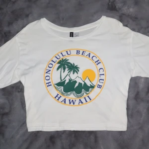 Vit Honolulu Beach Club t-shirt - Vit t-shirt med tryck av Honolulu Beach Club Hawaii. Den har korta ärmar och en avslappnad passform samt en kortare modell. Den är i bra skick!