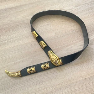 Svart bälte med gulddetaljer orm - Säljer ett snyggt svart ormbälte i skinn med coola gulddetaljer. Bältet har ett unikt mönster på spännet och ändarna, vilket ger det en lyxig känsla. Perfekt för att piffa upp vilken outfit som helst! Passar både till vardags och fest. 🖤✨längd 94 cm inklusive svans
