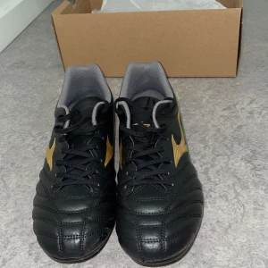Svarta fotbollsskor från Mizuno - Säljer ett par snygga svarta fotbollsskor från Mizuno i modellen Monarcida Neo. Dem är konstgrässkor! Om ni undrar hör av er bara till mig! Kan visa fler detaljer, Skorna har en stilren design med guldiga detaljer och är i mycket bra skick. Perfekta för fotbollsträningen eller match! Dem är har användes få gånger men har inte påverkat skorna alls!