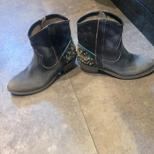 Svarta boots med nitar från Mexicana - Säljer ett par svarta boots från Mexicana i skinn med coola nitar i olika färger på hälen. De har en dragkedja på sidan för enkel på- och avtagning. Perfekta för en edgy look och passar både till vardags och fest. Använda men i bra skick.