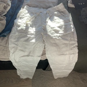 Vita linnebyxor från Zara - Säljer ett par vita linnebyxor från Zara i storlek S. De är superbekväma med elastisk midja och snörning för perfekt passform. Perfekta för en avslappnad dag hemma eller en snabb tur till affären. Byxorna är i bra skick och redo för en ny ägare!
