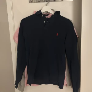 Mörkblå pikétröja från Ralph Lauren - Säljer en stilren mörkblå pikétröja från Ralph Lauren i slim fit. Tröjan har långa ärmar och klassisk krage med knappar. Perfekt för både vardag och lite finare tillfällen. Den är i mycket bra skick och redo för en ny ägare!