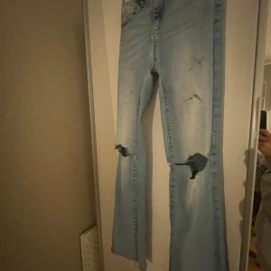 Ljusblå bootcut jeans - Säljer ett par ljusblå bootcut jeans i storlek 152. De har en cool slitning på knäna och en klassisk femficksdesign. Perfekta för en avslappnad stil med en touch av edge. Passar bra till både vardag och fest!