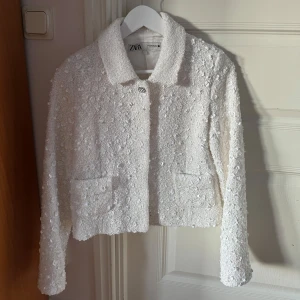 Vit kort jacka med paljetter från ZW Collection - Säljer en superfin vit jacka från ZW Collection. Den är kort och täckt med glittriga paljetter, perfekt för att lysa upp vilken outfit som helst. Jackan har en klassisk krage och långa ärmar. Jag har enbart använt den en gång och den är helt i nyskick💗😁
