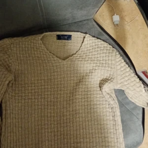 Beige stickad tröja från Armani Jeans - Säljer en superfin beige stickad tröja från Armani Jeans. Den har en snygg v-ringning och ett unikt vävt mönster som ger en cool textur. Perfekt för höst och vinter, och den är i mycket bra skick. Passar både till vardags och lite finare tillfällen. 🧶✨ Pris kan diskuteras. Kontakta för intresse 