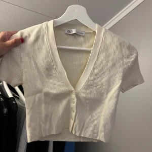 Topp Zara - Säljer en superfin beige ribbad topp från Zara i storlek S. Den har en v-ringad design med knappar framtill och korta ärmar. Toppen är i bra skick. Säljer för 60kr + frakt🥰