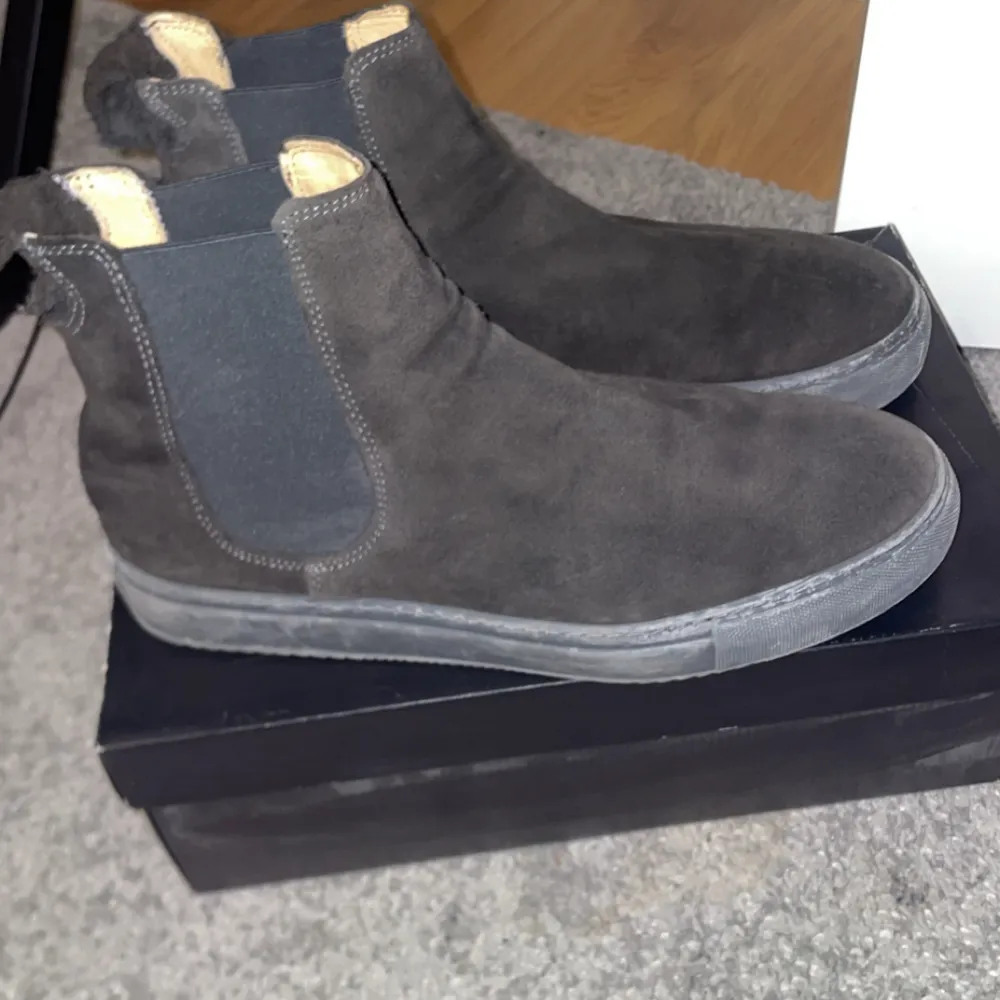 Säljer ett par snygga svarta Chelsea boots i mocka. De har en klassisk design med elastiska paneler på sidorna för enkel på- och avtagning. Perfekta för både höst och vår, och de ger en stilren touch till vilken outfit som helst. Skorna är i bra skick och redo för nya äventyr!. Skor.