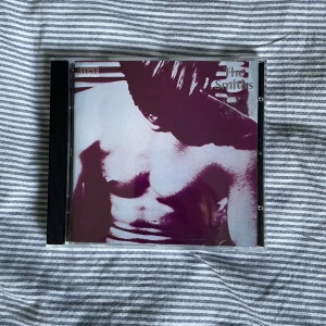The Smiths CD - Säljer en CD av The Smiths med ett ikoniskt omslag i lila och vitt. Skivan är i bra skick och kommer i ett klassiskt plastfodral. Perfekt för samlare eller fans av bandet!