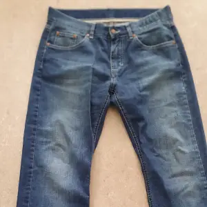 Säljer ett par klassiska blå jeans från Dressmann i storlek W34 L32. De är tillverkade i 100% bomull och har en traditionell femficksdesign med knapp och dragkedja. Perfekta för vardagsbruk och kan enkelt matchas med olika stilar. Passar bra för både höst och vår.