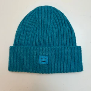 Turkos stickad mössa från Acne Studios - Säljer en snygg turkos stickad mössa från Acne Studios!💙 Den har en ribbad design. Perfekt för att hålla sig varm och stilren under kalla dagar. Passar både höst och vinter! Aldrig använd 