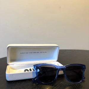 Chimi solglasögon - Snygga blå solglasögon i ett klassiskt wayfarer-stil. De har en cool, transparent blå båge och mörka linser som ger ett stilrent intryck. Perfekt för soliga dagar och kommer med ett praktiskt fodral för säker förvaring. Ett måste för sommaren!