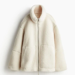 Vit teddyjacka med dragkedja - Mysig vit teddyjacka. Den har en dragkedja framtill och stora fickor för extra värme och stil. Jackan är långärmad och har en hög krage som skyddar mot vind. Perfekt för både höst och vinter!