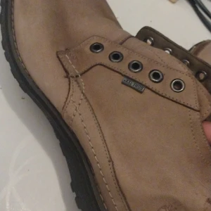 Beige skinnkängor från Timberland (Mocca) - Säljer ett par snygga och robusta beige kängor från Timberland i skinn. De har en klassisk design med snörning och en slitstark sula. Perfekta för höst och vinter, och de är i mycket bra skick. Passar både till vardags och lite mer uppklädda tillfällen. 1 par snören ingår åxå