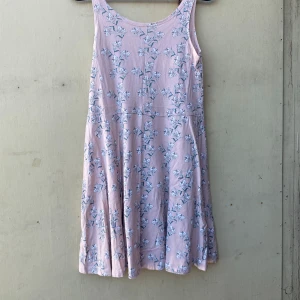 Ljusrosa blommig klänning - Säljer en superfin ljusrosa klänning med blommigt mönster. Den är ärmlös och perfekt för sommardagar. Klänningen har en skön passform och är gjord i ett mjukt material. Perfekt för både vardag och fest!