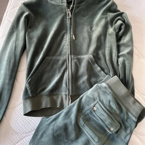 Grön velourjacka från Juicy Couture - Säljer en supermjuk och snygg grön velourjacka från Juicy Couture. Den har en dragkedja med ett stilrent J-hänge ( lite rostig men det märks ej) och praktiska fickor framtill. Perfekt för en avslappnad och trendig look