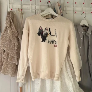 Beige stickad tröja från Ralph Lauren - Säljer en beige stickad tröja från Ralph Lauren med ett gulligt hundmotiv på framsidan. Tröjan har långa ärmar och ribbstickade muddar vid ärmslut och nederkant. Perfekt för en mysig dag!