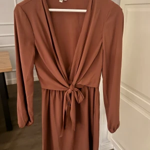 Brun klänning med knytning -  brun klänning med v-ringning och knytning i midjan. 