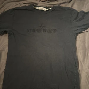 Svart t-shirt från Stone Island - Säljer en svart t-shirt från Stone Island med logotypen tryckt på bröstet. Perfekt för en stilren och avslappnad look.