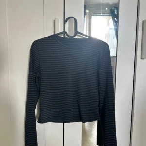 Svart och grå randig croppad tröja - Säljer en svart och grå randig croppad tröja med långa ärmar. Perfekt för en avslappnad stil.