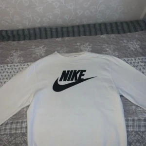 Vit långärmad tröja från Nike - Säljer en vit långärmad tröja från Nike med deras klassiska logga i svart på framsidan. Perfekt för en sportig och avslappnad stil. Tröjan är i storlek S och passar bra till både träning och vardag.