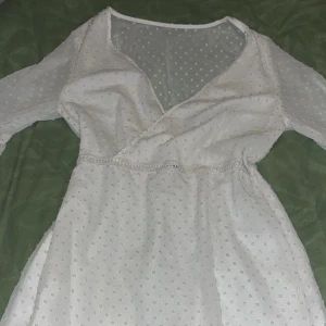 Vit prickig klänning från Shein - Säljer en söt vit klänning från Shein med prickigt mönster och omlott-design. Klänningen har trekvartsärmar och volangdetaljer som ger en romantisk känsla. Perfekt för vår och sommar!