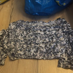 Blommig topp från Uniq Young  - Säljer en söt blommig topp från Only med volangdetaljer. Toppen har en mörkblå och vit färgkombination och är perfekt för en somrig look. Den är kortärmad och har en elastisk passform.