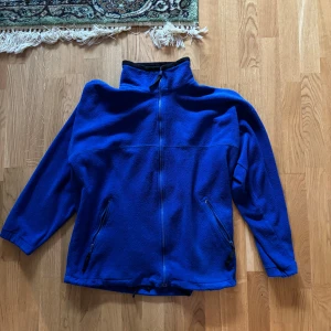 Blå fleecejacka från Cavo - Säljer en blå fleecejacka från Cavo med dragkedja framtill. Jackan har en hög krage och två fickor med dragkedjor. Perfekt för kyliga dagar.