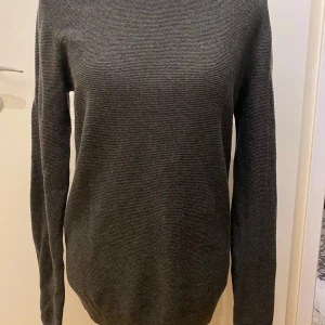 Grå stickad tröja från Calvin Klein Jeans - Säljer en stilren grå stickad tröja från Calvin Klein Jeans. Tröjan har en klassisk rund halsringning och långa ärmar, perfekt för kyligare dagar. Enkel och tidlös design som passar till det mesta.  Längd: 73 cm Armhåla till armhåla: 49 cm 84% bomull, 16% ull  Inga bilder när den sitter på mig! Katter finns i hemmet