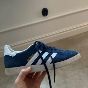 Blå Adidas Gazelle sneakers - Säljer ett par klassiska Adidas Gazelle sneakers i blå mocka med vita detaljer och snörning. Väldig bra skick använda ungefär 5 gånger 