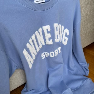 Blå sweatshirt från Anine Bing - Säljer en snygg blå sweatshirt från Anine Bing med texten 'ANINE BING SPORT' i vitt på framsidan. Perfekt för en avslappnad stil. Använd enstaka gång. Storlek L men oversize s på mig