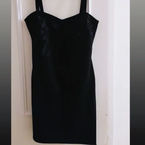 Svart klänning från Freequent - Elegant svart klänning från Freequent med breda axelband och en figurnära passform. Perfekt för en stilren look. Klänningen har en subtil struktur i tyget som ger en extra dimension.