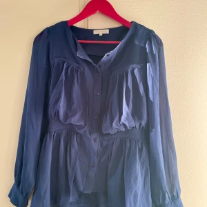 Mörkblå blus från Version Originale - Elegant mörkblå blus med långa ärmar och knappar framtill. Blusen har en luftig passform med fina detaljer som ger en stilren look. Perfekt för både vardag och speciella tillfällen.