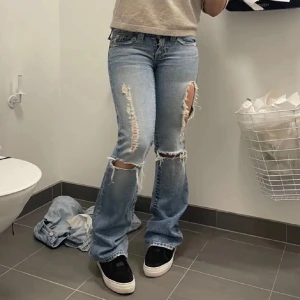 Blå slitna truereligion jeans - Säljer ett par blåa truereligion jeans med slitningar och hål på knäna. De har en bootcut-stil och är lågmidjade. Perfekta för en avslappnad look. De är verkligen så fina men de passar inte längre och behöver rensa ut min garderob 😍💕har lite slitage längst ner pga att de är lite upptrampade 