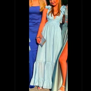 Ljusblå  balklänning med volanger - Säljer min så fina ljusblå balklänning med volangdetaljer och blomaktiga axelband. Köpt i Spanien på en balklänningsbutik i storlek S men skulle säga att den är mer åt XS dock justerbar med knytningen i ryggen. Perfekt för att kunna ha en unik klänning. Superbra skick och endast använd vid ett tillfälle. Bara att höra av sig om man har några frågor eller vill se fler bilder.💕