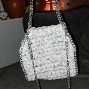 Vit/grå spräcklig virkad väska med kedjedetaljer - Snygg vit/grå spräcklig virkad väska med silverfärgade kedjedetaljer. Perfekt för att ge din outfit en unik touch. Väskan har en rektangulär form och är både stilren och praktisk.
