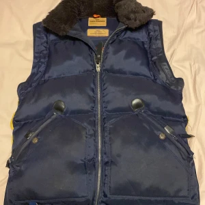  Parajumpers väst - Säljer en snygg mörkblå dunväst från Parajumpers med dragkedja och flera praktiska fickor. Västen har en mjuk krage i äkta päls och är perfekt för kyligare väder. Den är både stilren och funktionell.