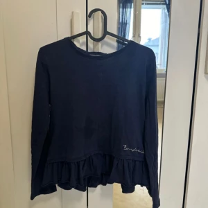 Mörkblå tröja med volangdetalj - Snygg mörkblå tröja från By Malene Birger med volangdetalj vid nederkanten. Tröjan har långa ärmar och en rund halsringning. Perfekt för en stilren look.