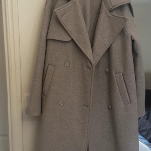 Beige kappa från NA-KD - Snygg beige kappa från NA-KD med dubbelknäppning och breda slag. Perfekt för kyligare dagar med sin stilrena design och praktiska fickor. 