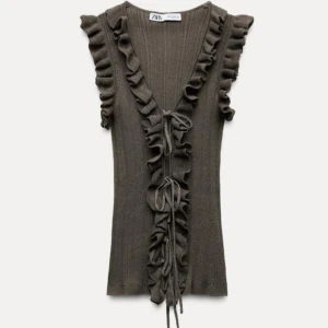 Khaki färgad ribbad topp med volangdetaljer från Zara.  - Snygg khaki färgad ribbad topp från Zara med volangdetaljer längs ärmhålen och fram. Toppen har en knytning framtill och är ärmlös, perfekt för lager-på-lager eller som den är. Helt oanvänd bara provad, intakt prislapp. 