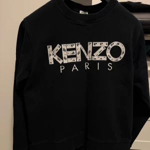 Svart sweatshirt från Kenzo Paris - Säljer en stilren svart sweatshirt från Kenzo med deras ikoniska logga i vitt på framsidan. Tröjan har långa ärmar och en klassisk rund halsringning. Perfekt för en avslappnad och trendig look. Köpt på NK i Stockholm, kvitto finns. Passar M. 