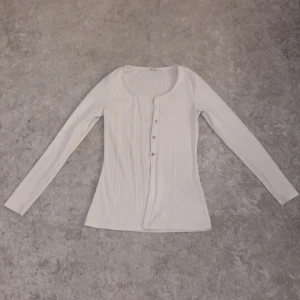 Vit ribbad långärmad topp - Tjejkläder!, Säljer en stilren vit ribbad topp med långa ärmar och knappar framtill. Perfekt för en enkel och snygg look. Passar bra till både jeans och kjol.