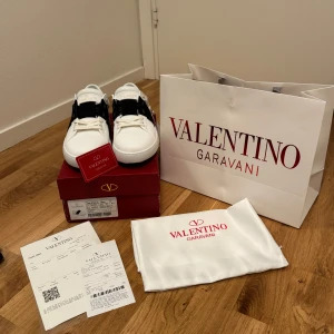 Valentino Garavani sneakers - Snygga Valentino Garavani sneakers storlek 42 i vitt med en bred svart rem över ovansidan. Skorna har en stilren design med snörning och är tillverkade i skinn. Perfekta för en trendig look. Prisen är 1499 kan diskutera prisen vid  snabba affär. 