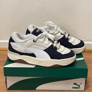 Puma sneakers i marinblå och vit - Snygga Puma sneakers i marinblå och vit med klassisk design. Skorna har snörning och en bekväm passform, perfekt för vardagsbruk. De kommer i originalkartong.
