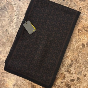 Brun halsduk från Fendi - Fendi halsduk i brunt o svart med Fendi-logotypen. Ull  Halsduken är ny och oanvänd, med alla originaltaggar kvar.   (Taggen är av då jag ville ha den på mig men halsduken levde inte upp till mina förväntningar om längd och färg till mitt ytterplagg)