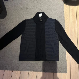 Marinblå jacka från ICE - Snygg marinblå jacka från ICE med quiltad framsida och stickade ärmar. Jackan har en hög krage och stängs med dragkedja. Perfekt för kyligare dagar. Skriv vid frågor och funderingar 